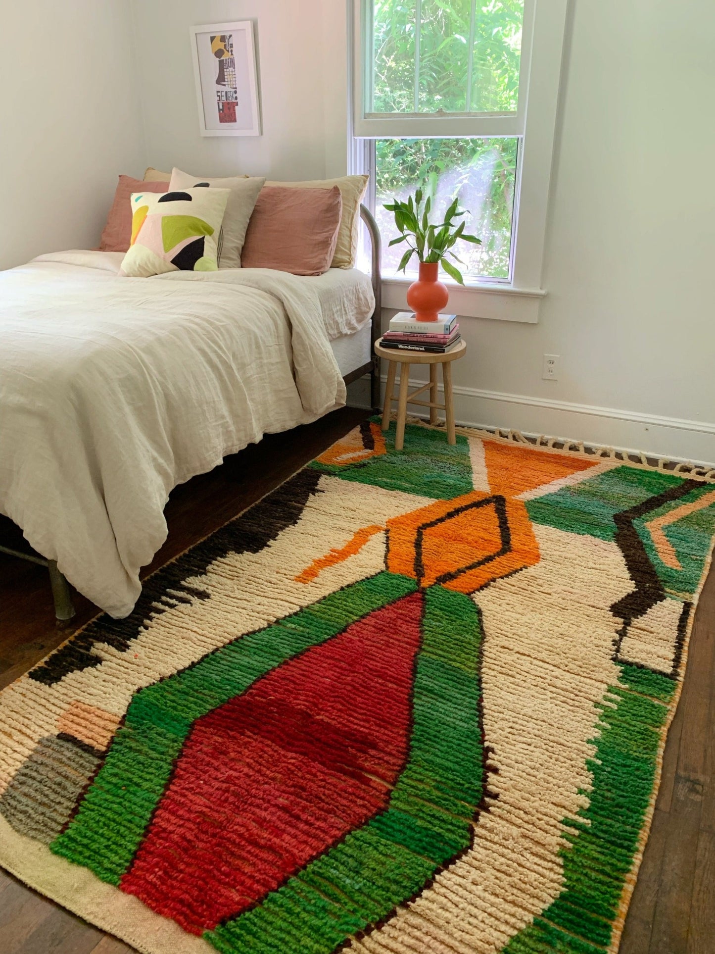 Grassy green, cream, carmine, and tangerine abstract Moroccan rug looks lovely next to an orange vase of lillies.